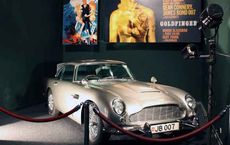 Classic silver car displayed at an exhibition with movie posters and camera, featured on digipdemo.com's Iconic Movie Cars article.