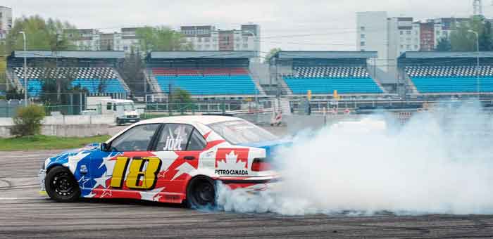 "Car performing a high-speed drift on a racetrack, producing a cloud of smoke, at a drifting event on digipdemo.com."